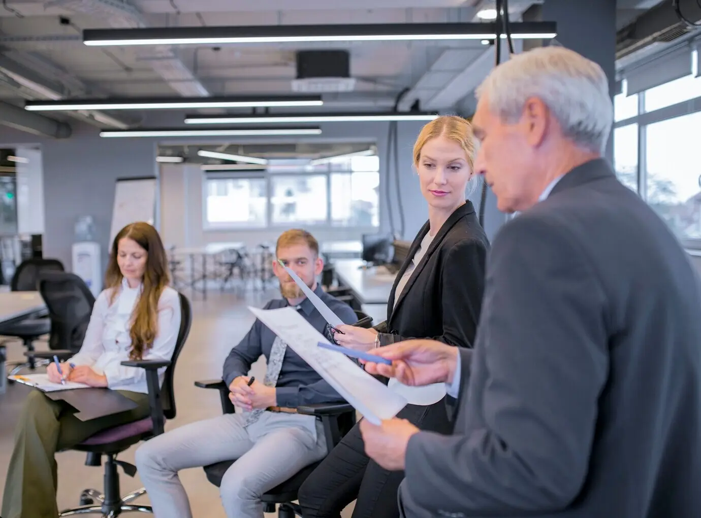 Eine junge Geschäftsfrau schaut einen älteren Geschäftsmann an, der auf die Dokumente in seiner Hand zeigt.